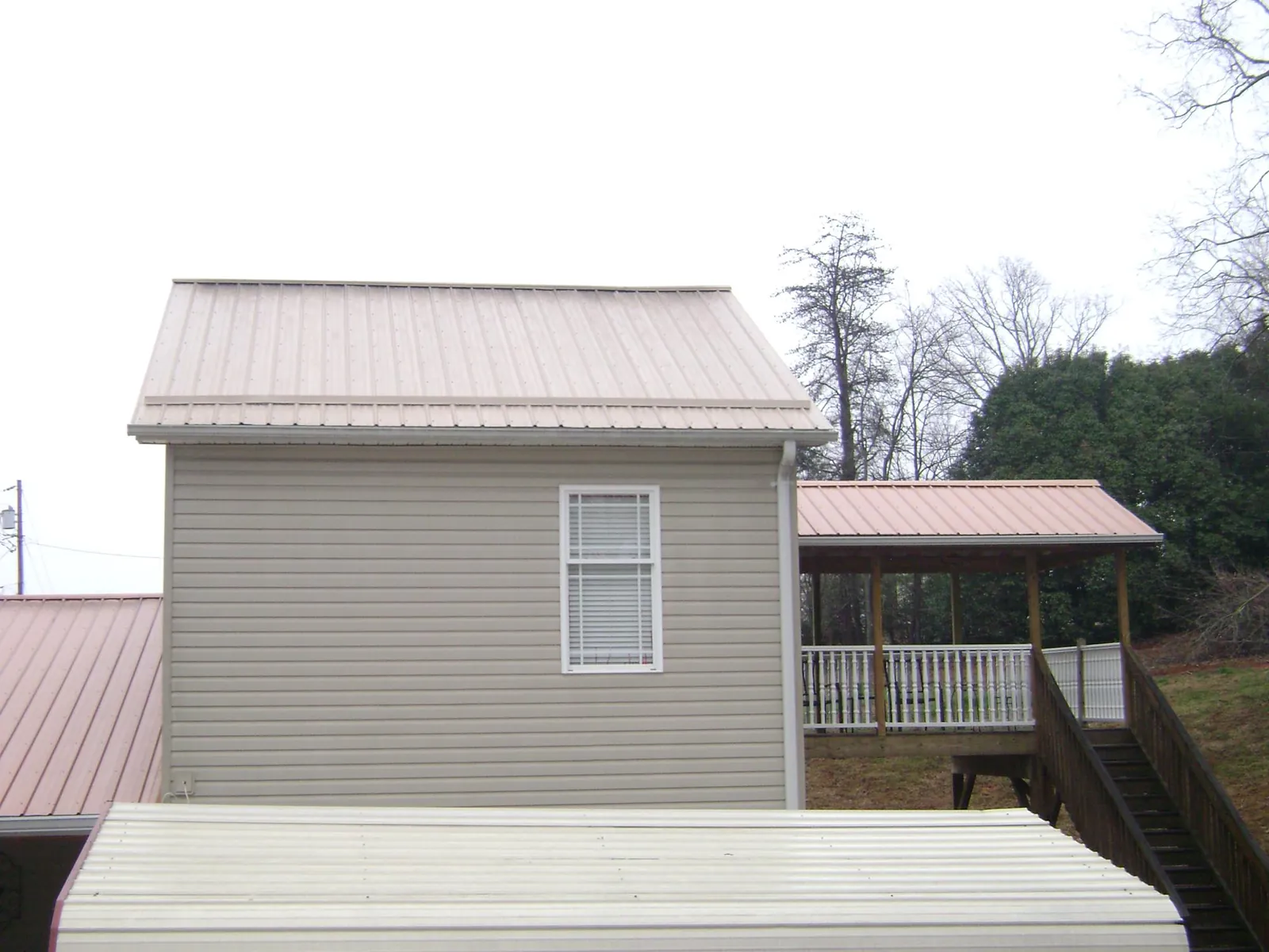 Tan metal roofs on a two story addition and attached porch, from a Roof Replacement job in Joseph